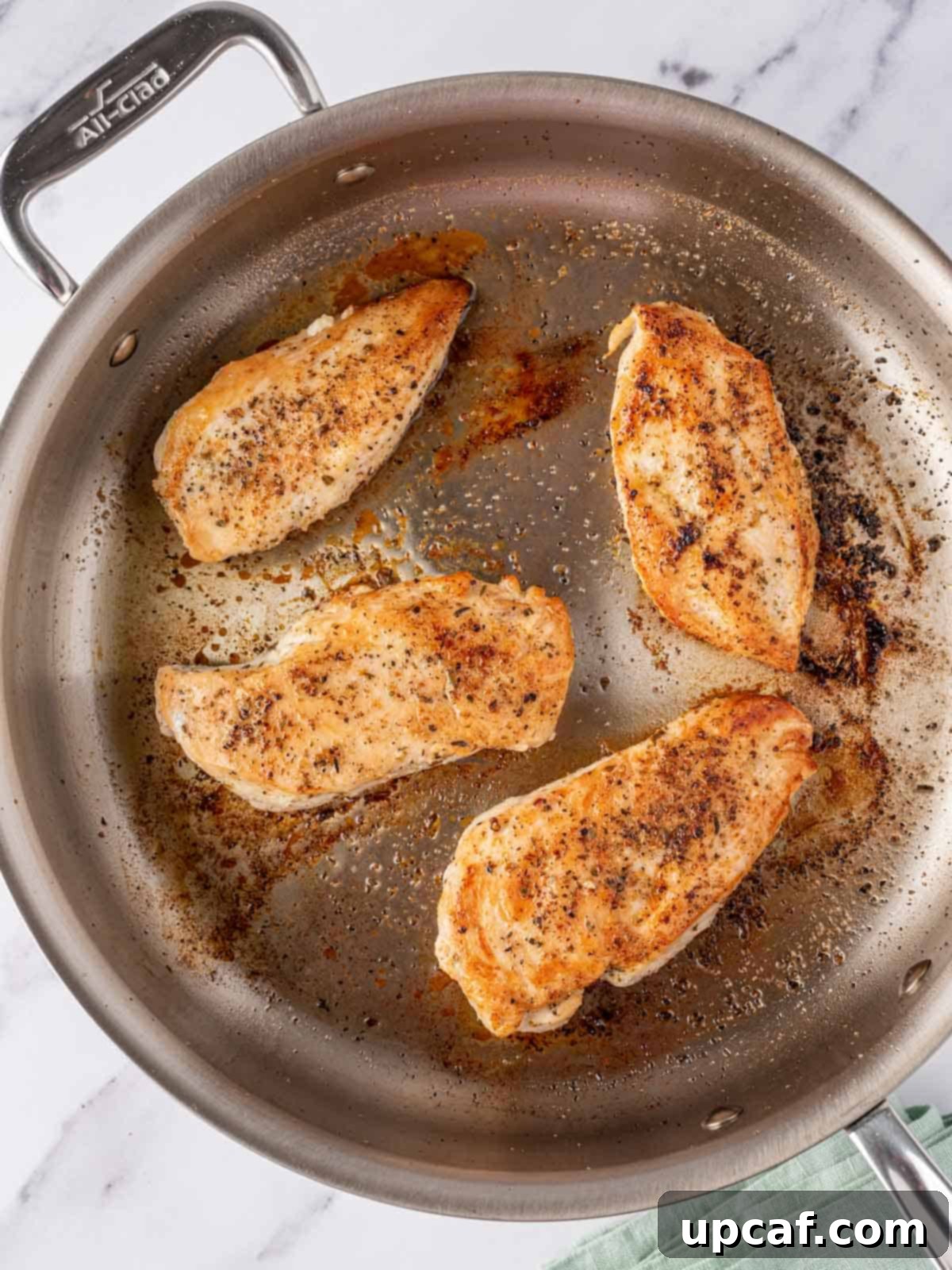Overhead view of chicken breasts searing in a hot skillet, developing a golden crust.