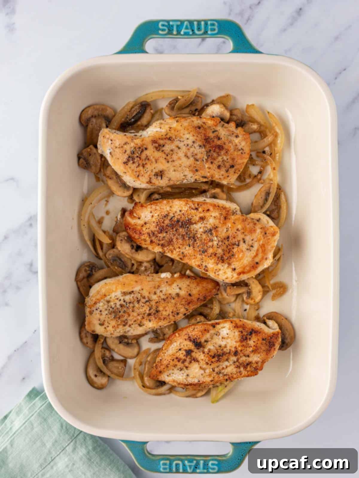 Seared chicken breasts placed on a layer of sautéed mushrooms in a blue baking dish.