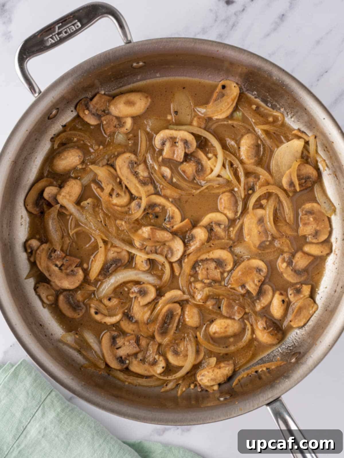 Sautéed mushroom mixture simmering with chicken broth in a skillet.