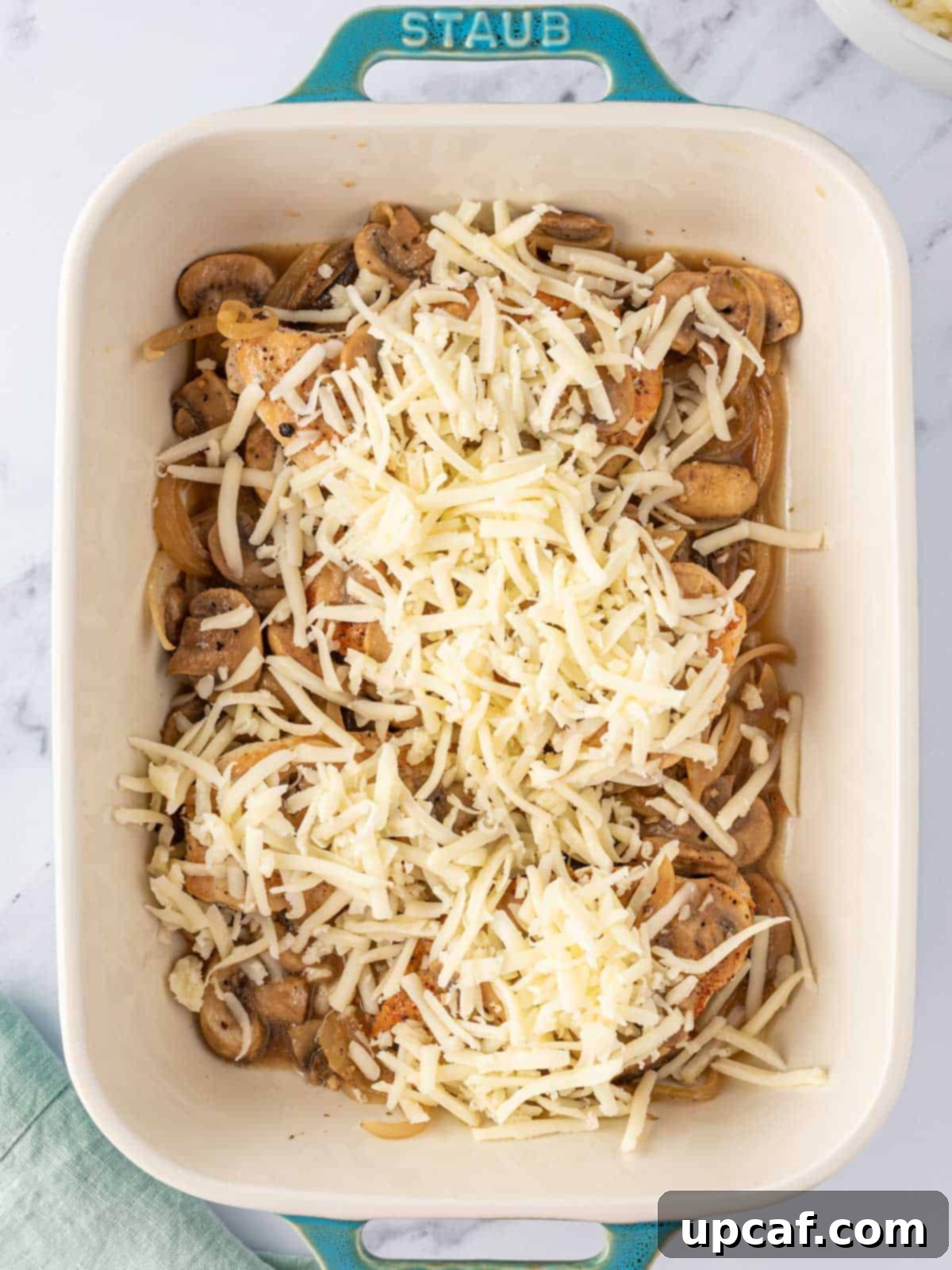 Shredded mozzarella cheese generously sprinkled over the chicken and mushrooms in the baking dish.