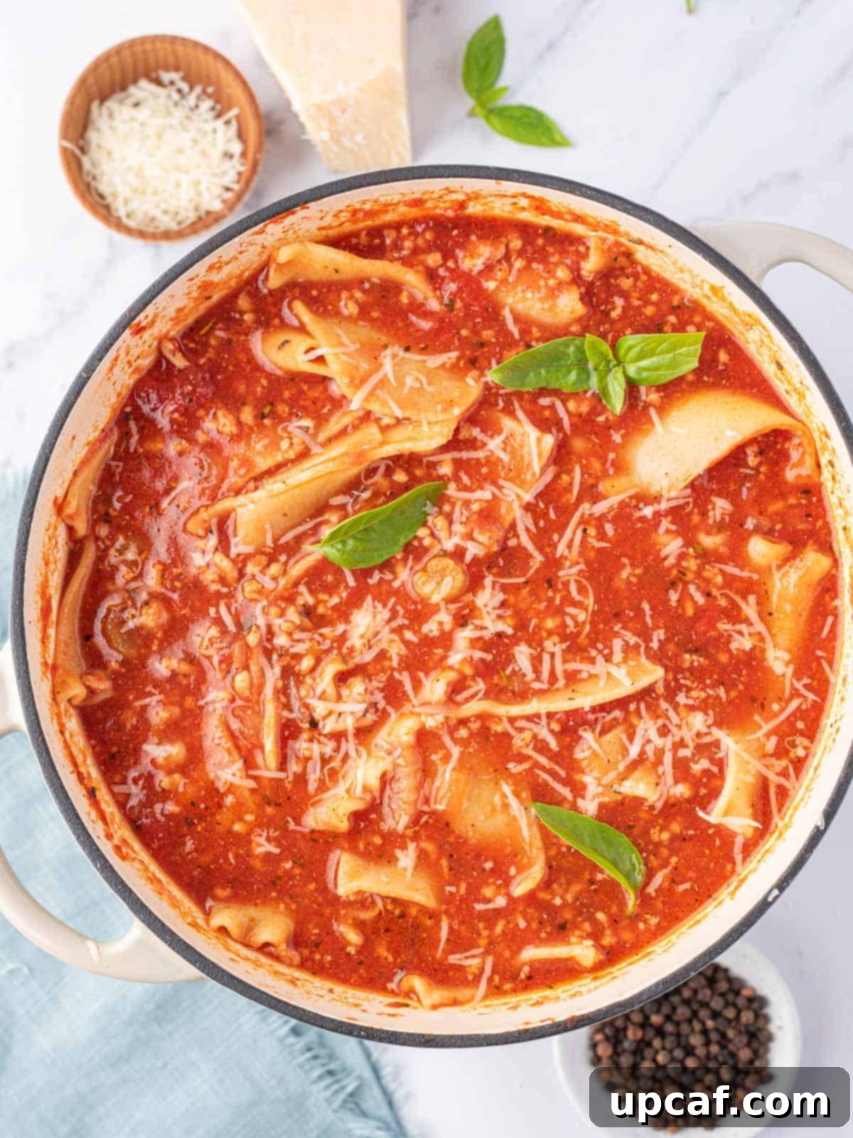 A top view of one pot lasagna soup with a few leaves of green basil and a small bowl of parmesan cheese to the side.