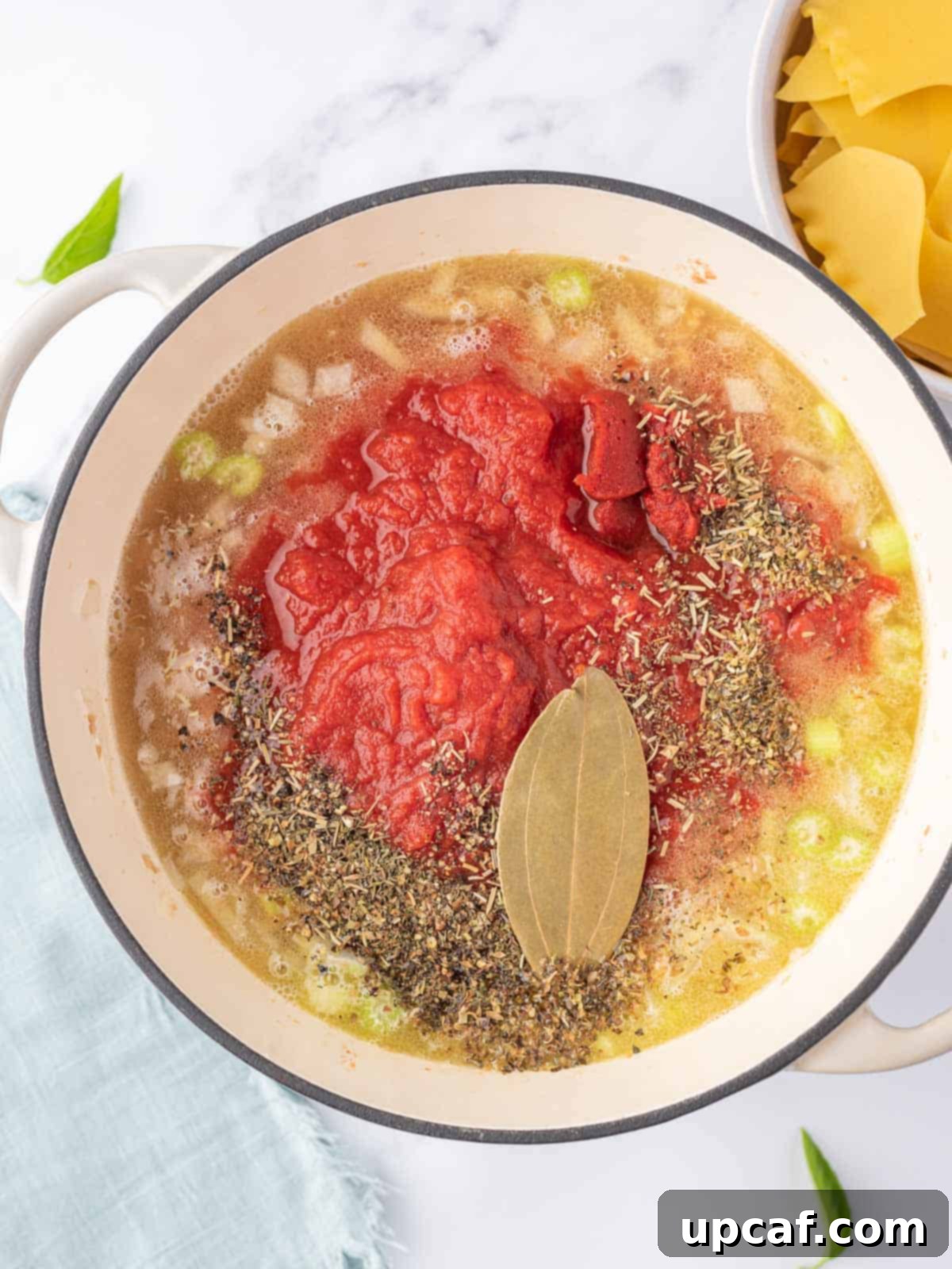 Process photo for making the broth with crushed tomatoes, herbs and spices and a bay leaf.