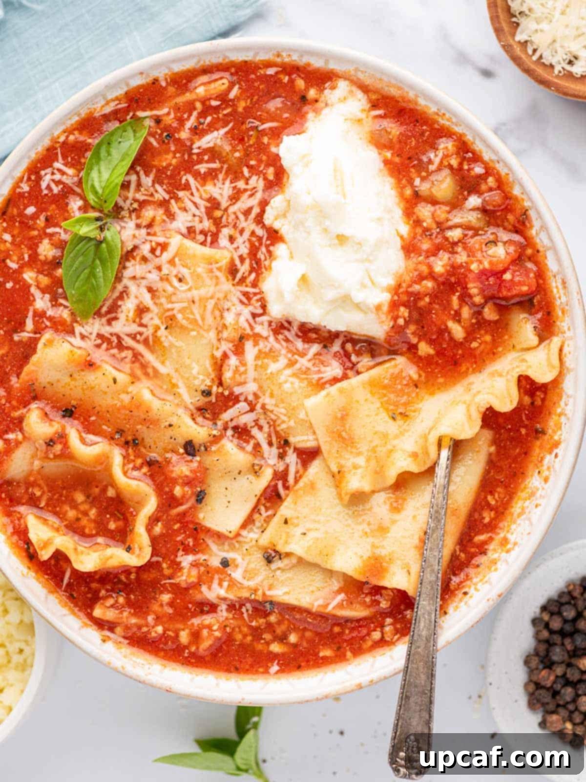 A silver spoon in a bowl of easy lasagna soup with basil leaves, parmesan cheese and a dollop of ricotta cheese.