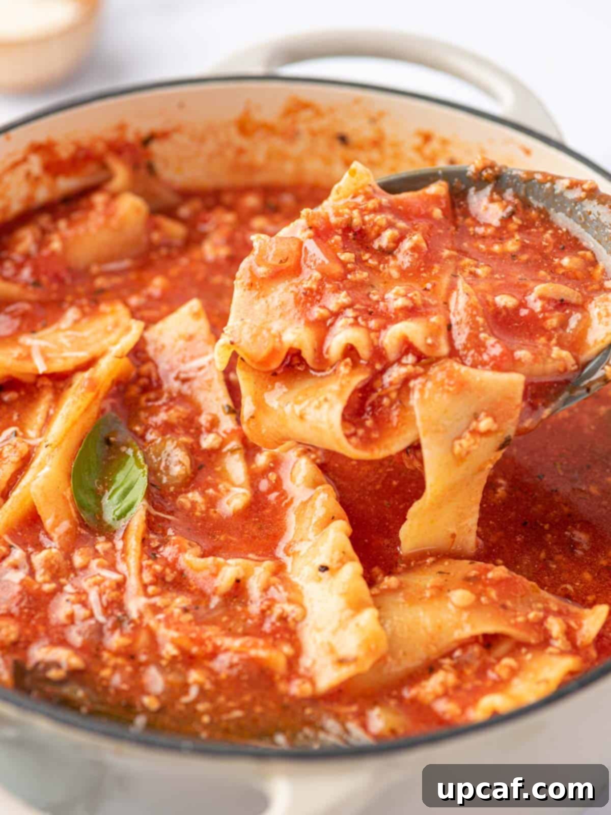 A ladle is being used to scoop noodle and tomato broth out of a white enameled dutch oven filled with easy lasagna soup.