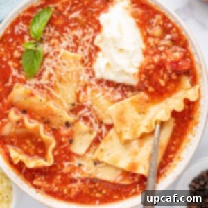 A silver spoon in a bowl of easy lasagna soup with basil leaves, parmesan cheese and a dollop of ricotta cheese.