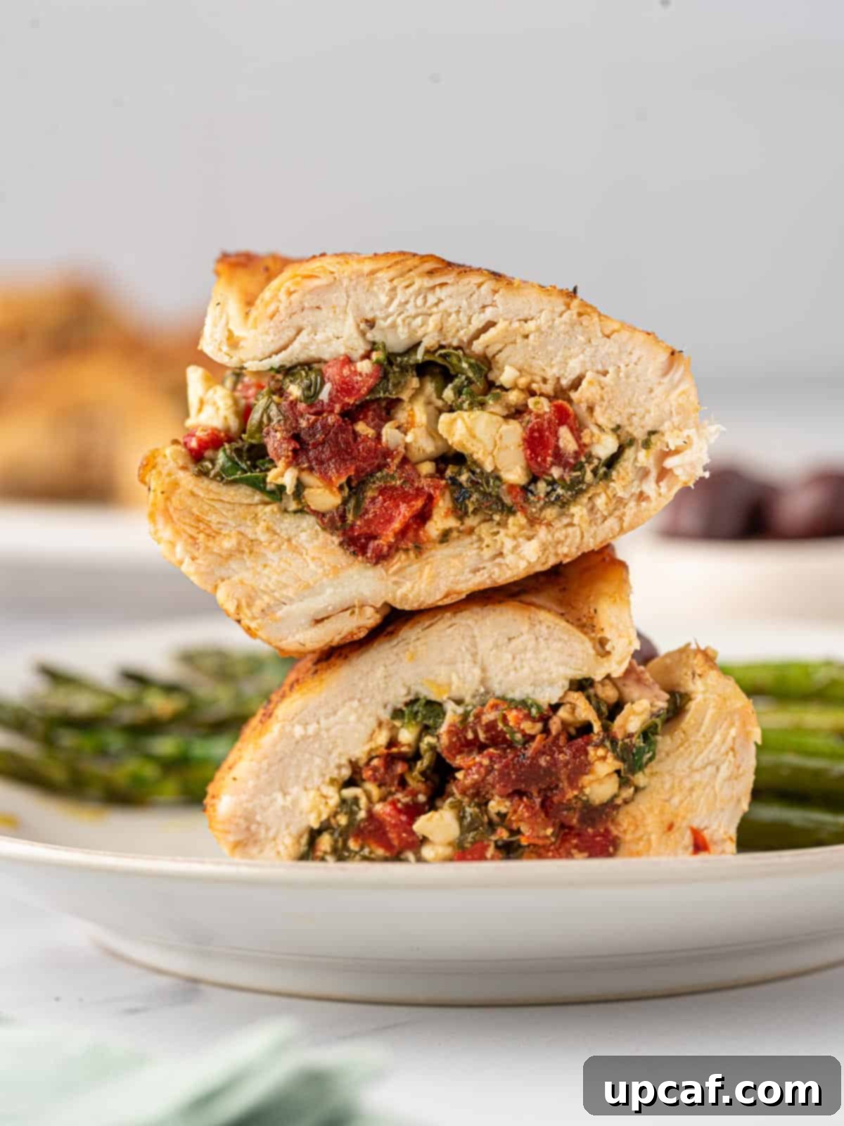 Sun-Drenched Mediterranean Stuffed Chicken 2 Two halves of a Mediterranean stuffed chicken breast stacked on top of each other, garnished with fresh herbs.