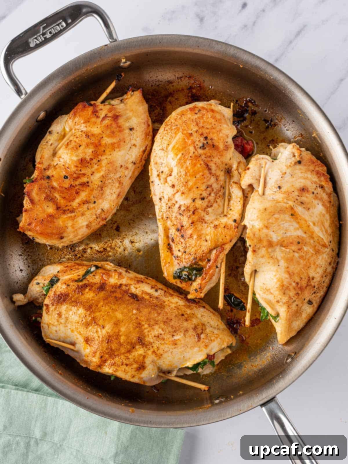 Sun-Drenched Mediterranean Stuffed Chicken 7 Mediterranean stuffed chicken breasts searing in an oven-safe pan.