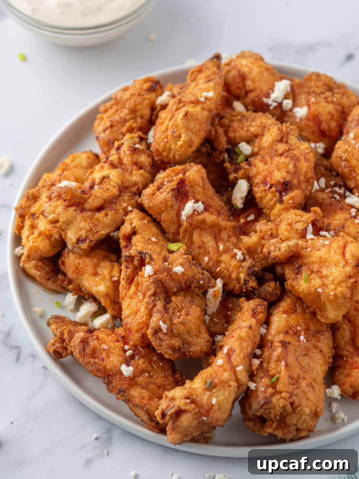 KFC's Fiery Nashville Chicken Tenders 2 A plate of Nashville hot chicken tenders with crumbled cheese and pickles, ready to be served.