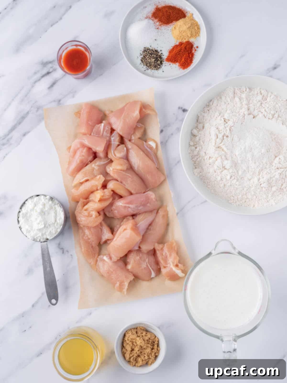 KFC's Fiery Nashville Chicken Tenders 3 A flat lay of all the ingredients needed to prepare Nashville hot chicken tenders, including chicken, buttermilk, spices, and oil.