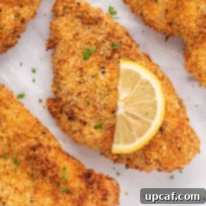 Closeup of a crispy chicken cutlet with a lemon slice on top.