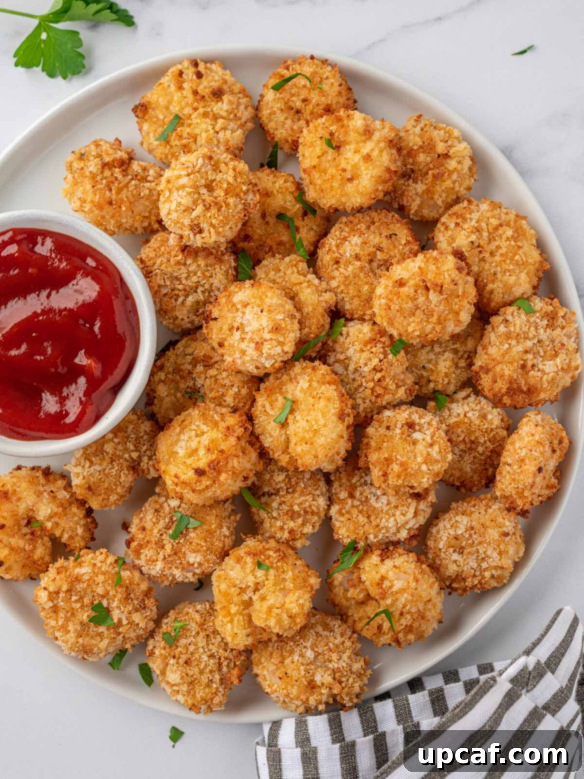 A white tray of air fryer popcorn shrimp with a small bowl of cocktail sauce, garnished with fresh parsley.