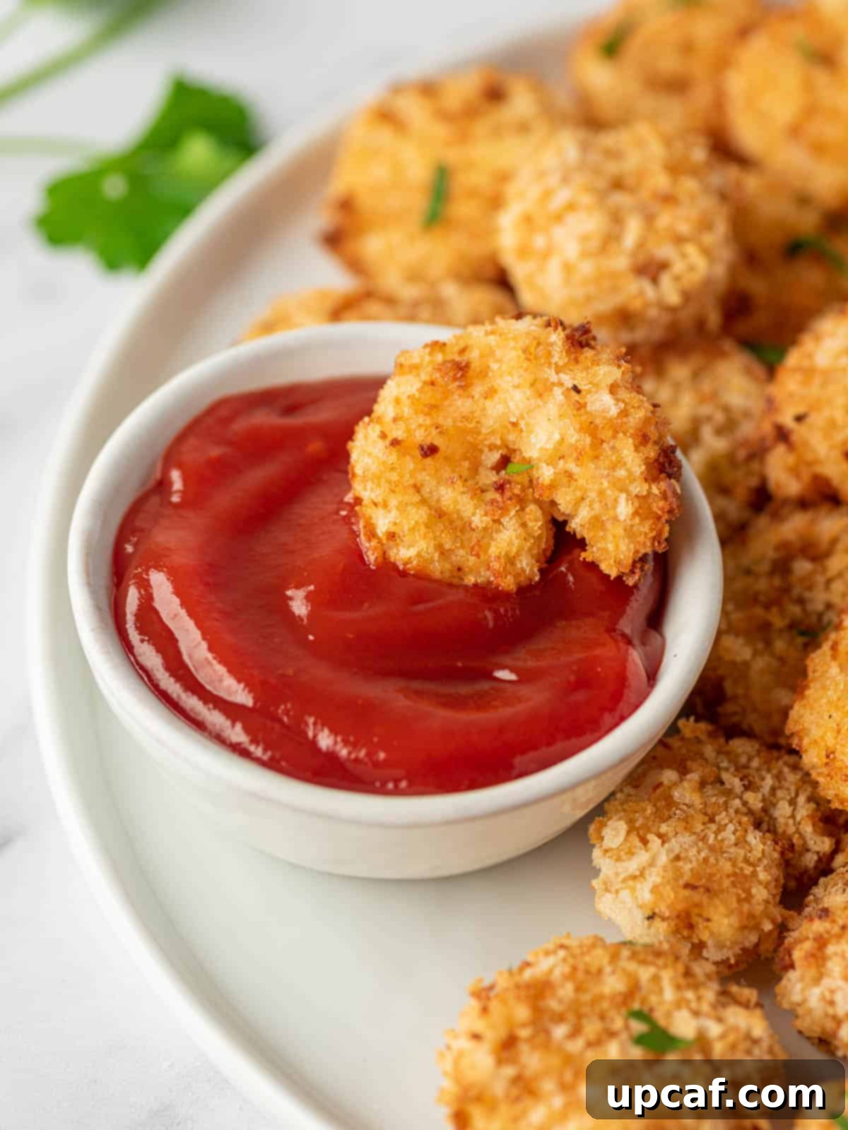 A piece of air fryer popcorn shrimp is dipped into a small bowl of cocktail sauce, ready to be enjoyed.