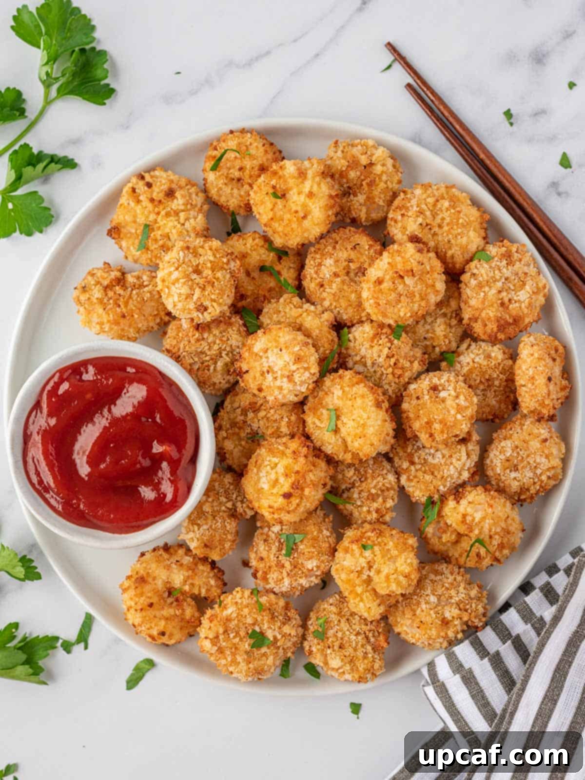 Cooked popcorn shrimp recipe on a round white tray with a bowl of dipping sauce and fresh parsley.