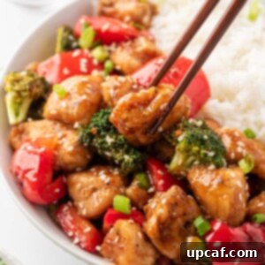 Chopsticks gracefully picking up a piece of Teriyaki Chicken Stir Fry from a bowl of steamed rice, symbolizing a delicious meal.