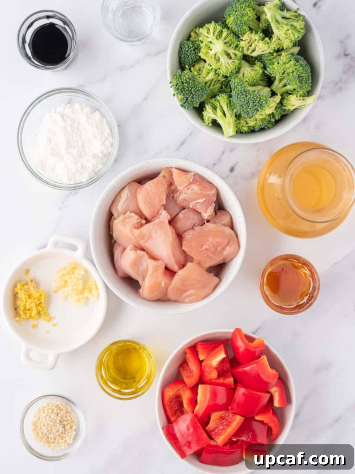 Several small white bowls containing fresh ingredients for an easy chicken teriyaki stir fry recipe, including diced chicken, chopped bell peppers, broccoli florets, and sauce components.