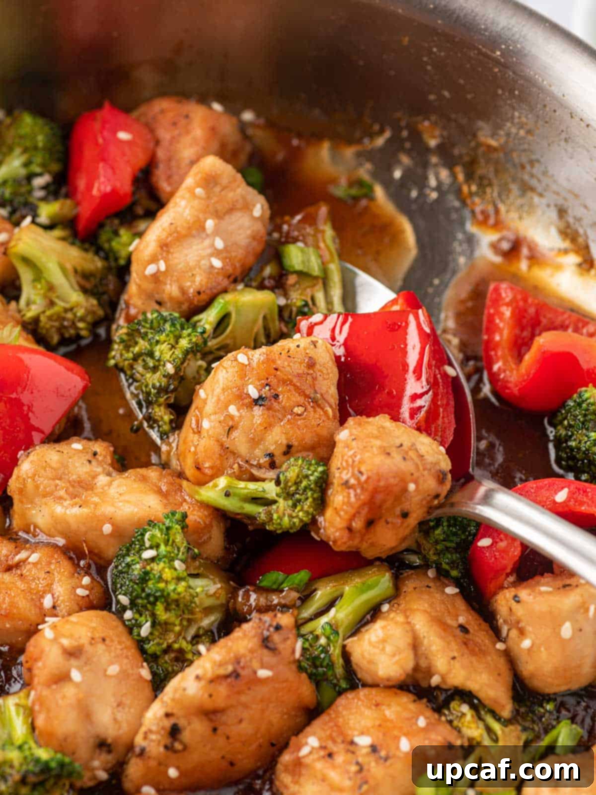 A spoon lifting a piece of easy chicken teriyaki stir fry from the skillet, showcasing the rich sauce and vibrant ingredients.