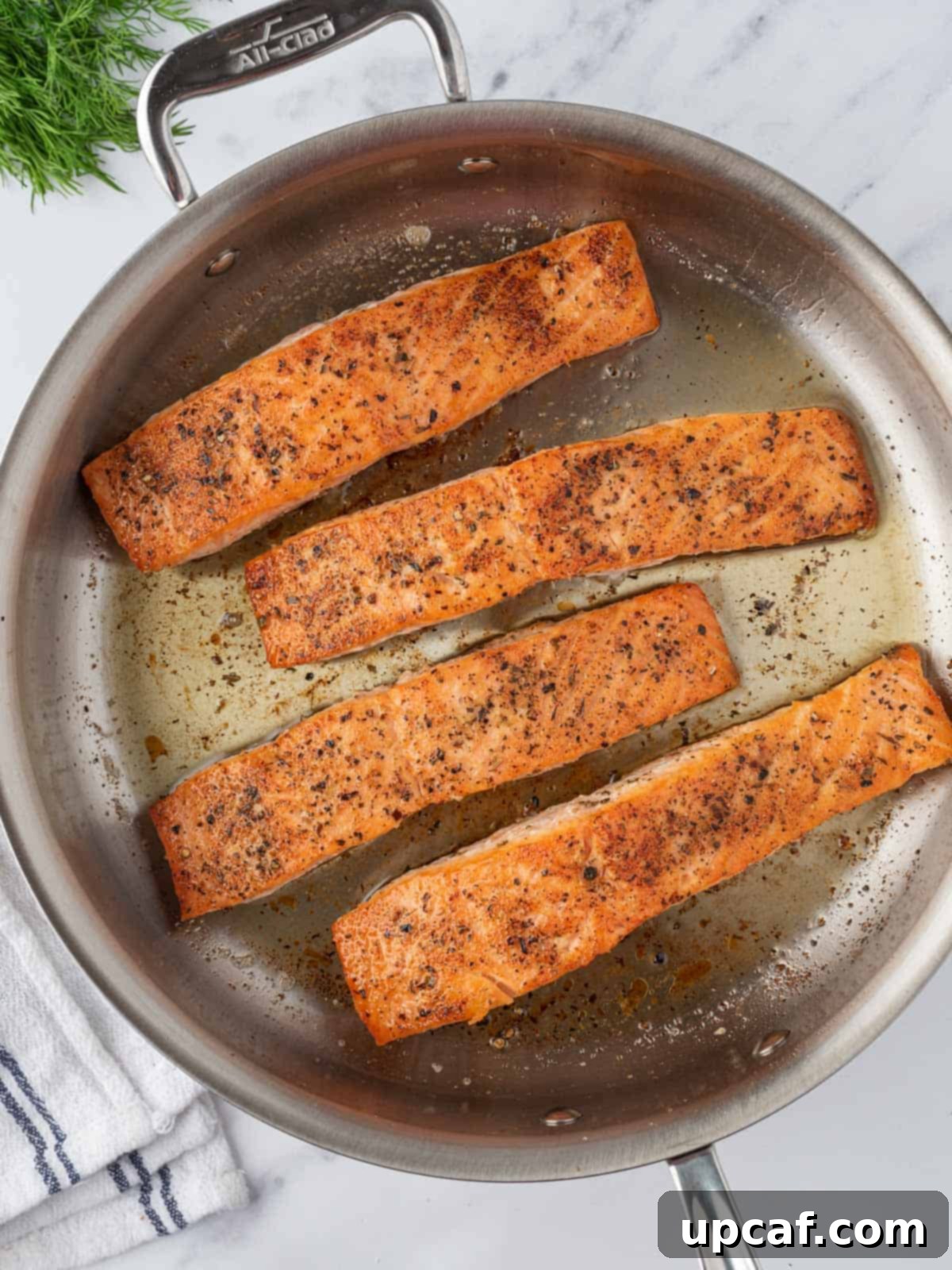 Two salmon fillets searing in a hot skillet, developing a golden-brown crust.