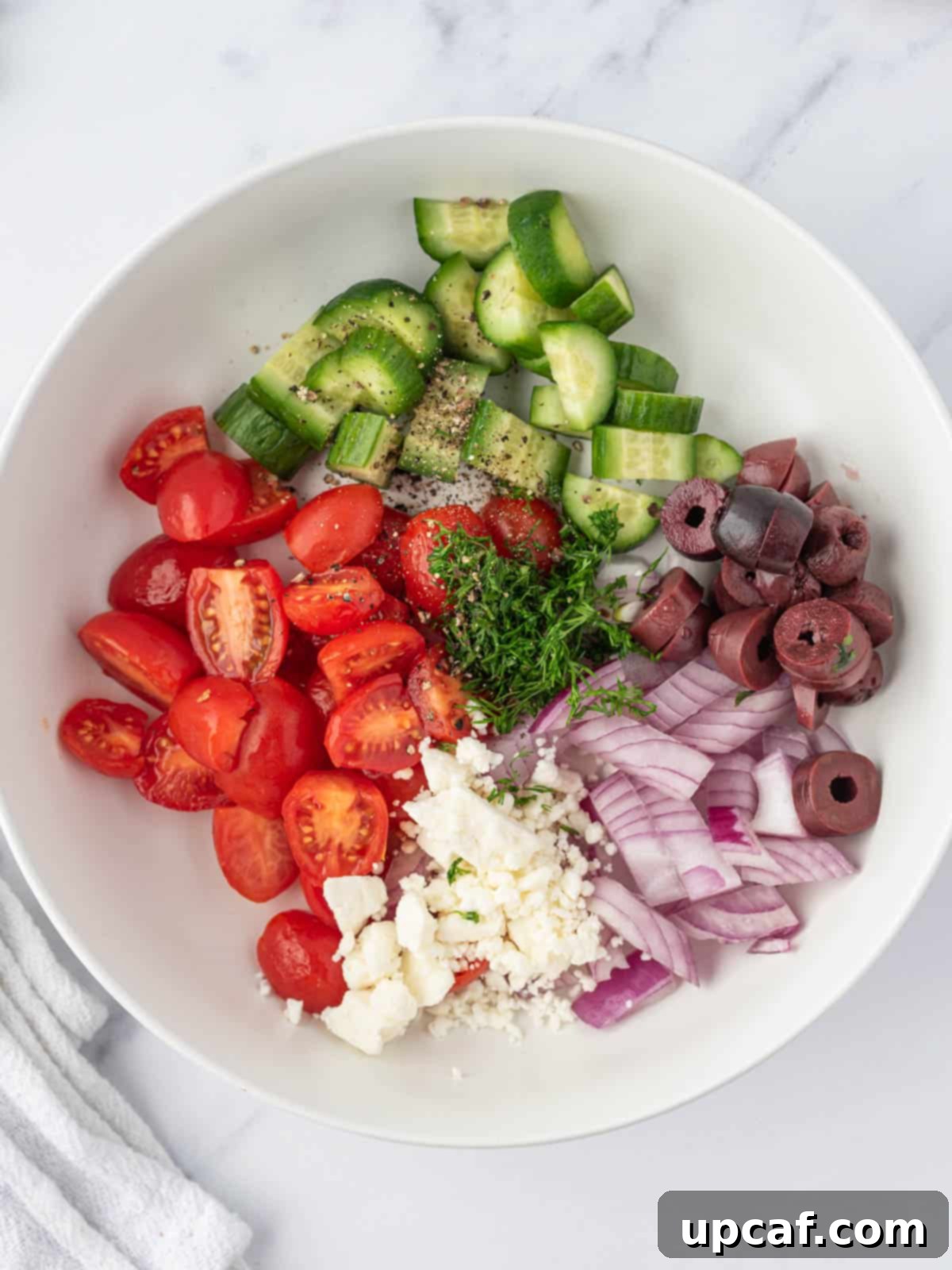 A bowl filled with freshly chopped vegetables for the Greek salsa, including tomatoes, cucumber, red onion, and olives.