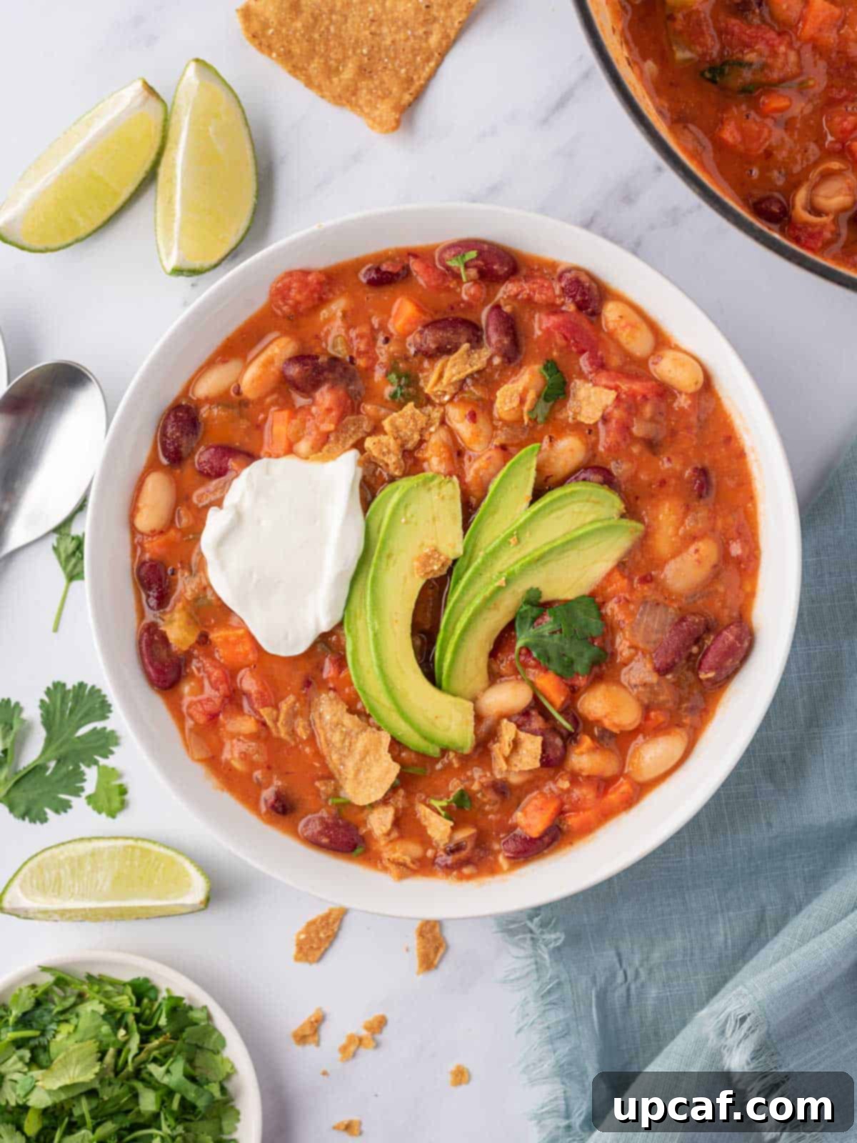 A bowl of easy vegan chili garnished with creamy avocado slices, fresh cilantro, and a dollop of vegan sour cream, presenting a vibrant and appetizing meal.