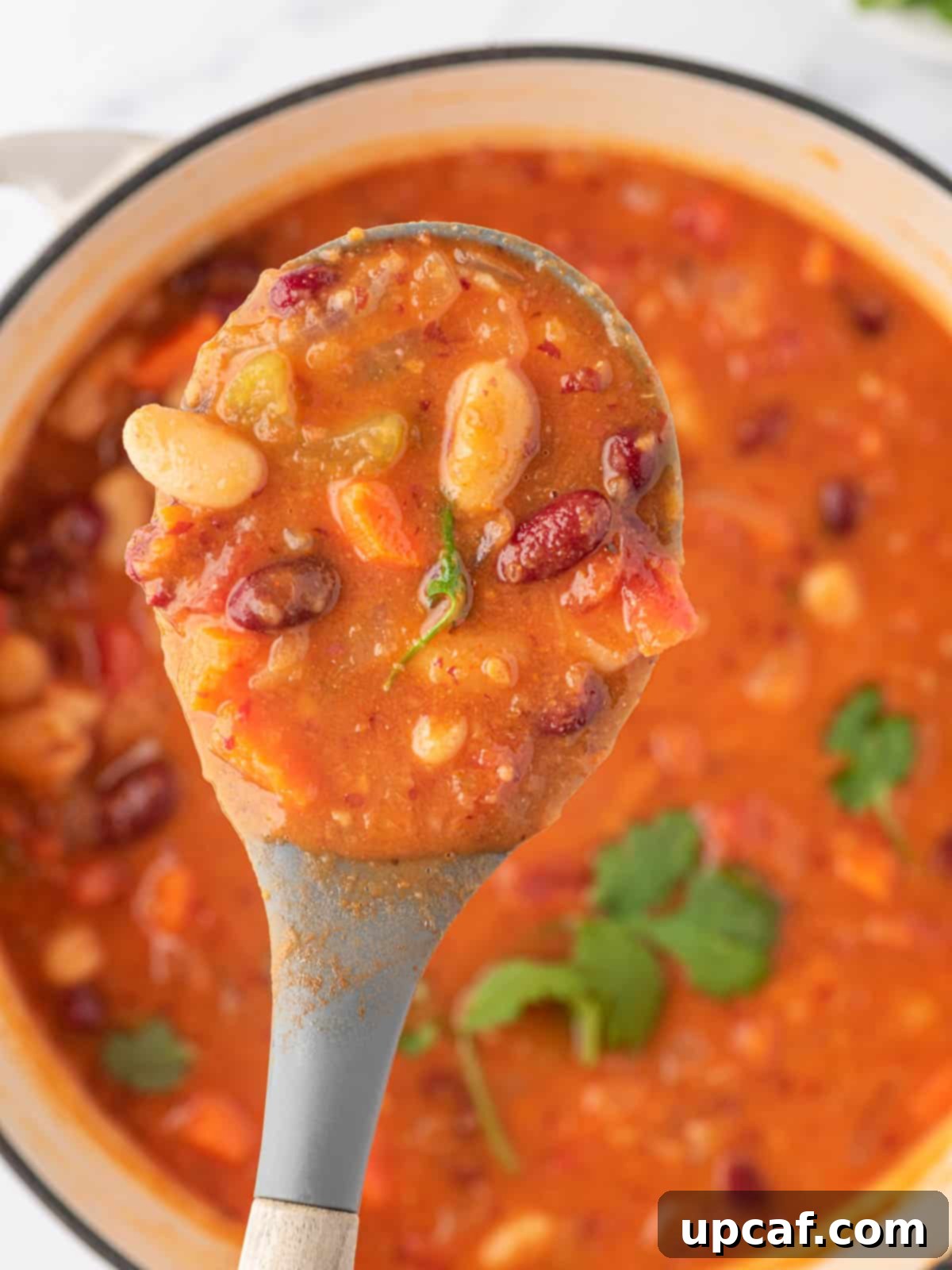 A spoonful of rich kidney bean chili being lifted from a full, steaming pot, showcasing its hearty texture and deep color.