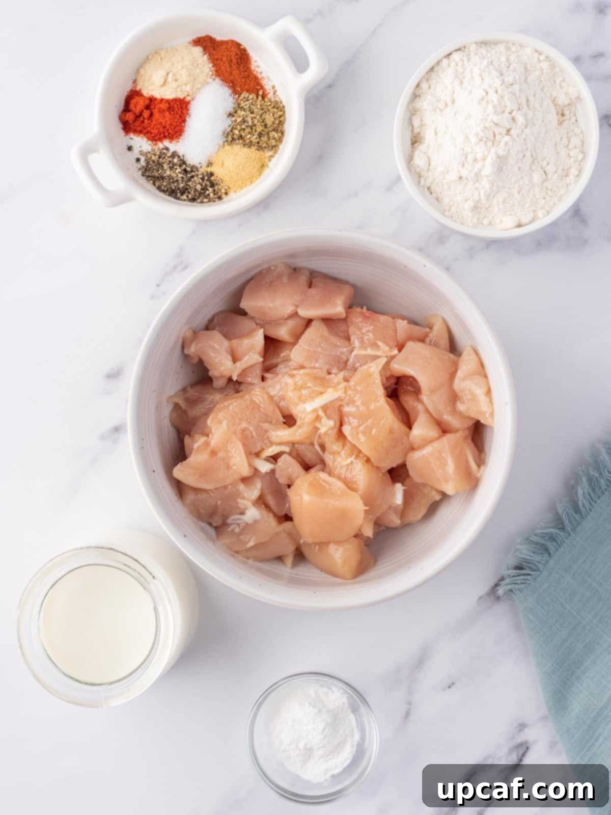A collection of fresh ingredients laid out, including chicken, buttermilk, flour, and various spices, ready for preparing fried popcorn chicken.