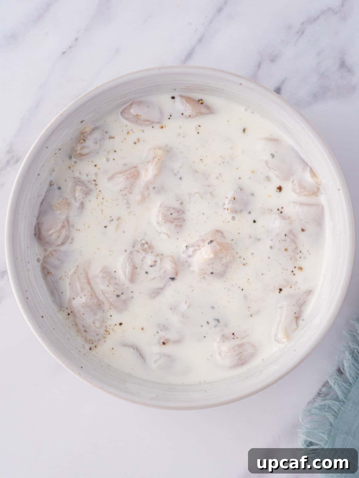 Close-up of raw chicken nuggets marinating in a bowl of seasoned buttermilk, showing the preparation stage for homemade popcorn chicken.