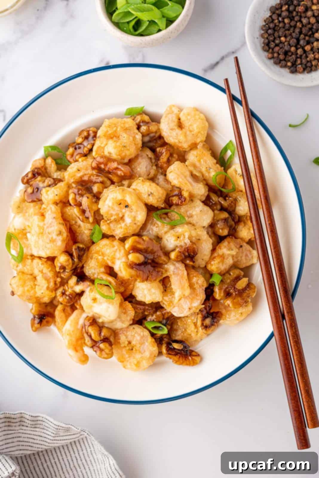 A beautifully arranged bowl of Honey Walnut Shrimp, garnished with fresh scallions, with chopsticks ready for serving. The shrimp are golden and crispy, coated in a creamy sauce, alongside shiny candied walnuts.