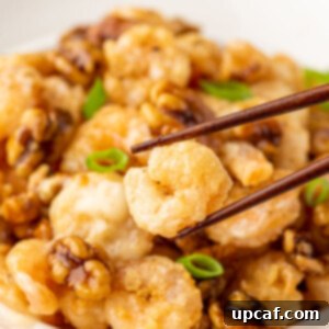 Chopsticks picking up a piece of Honey Walnut Shrimp from a bowl.