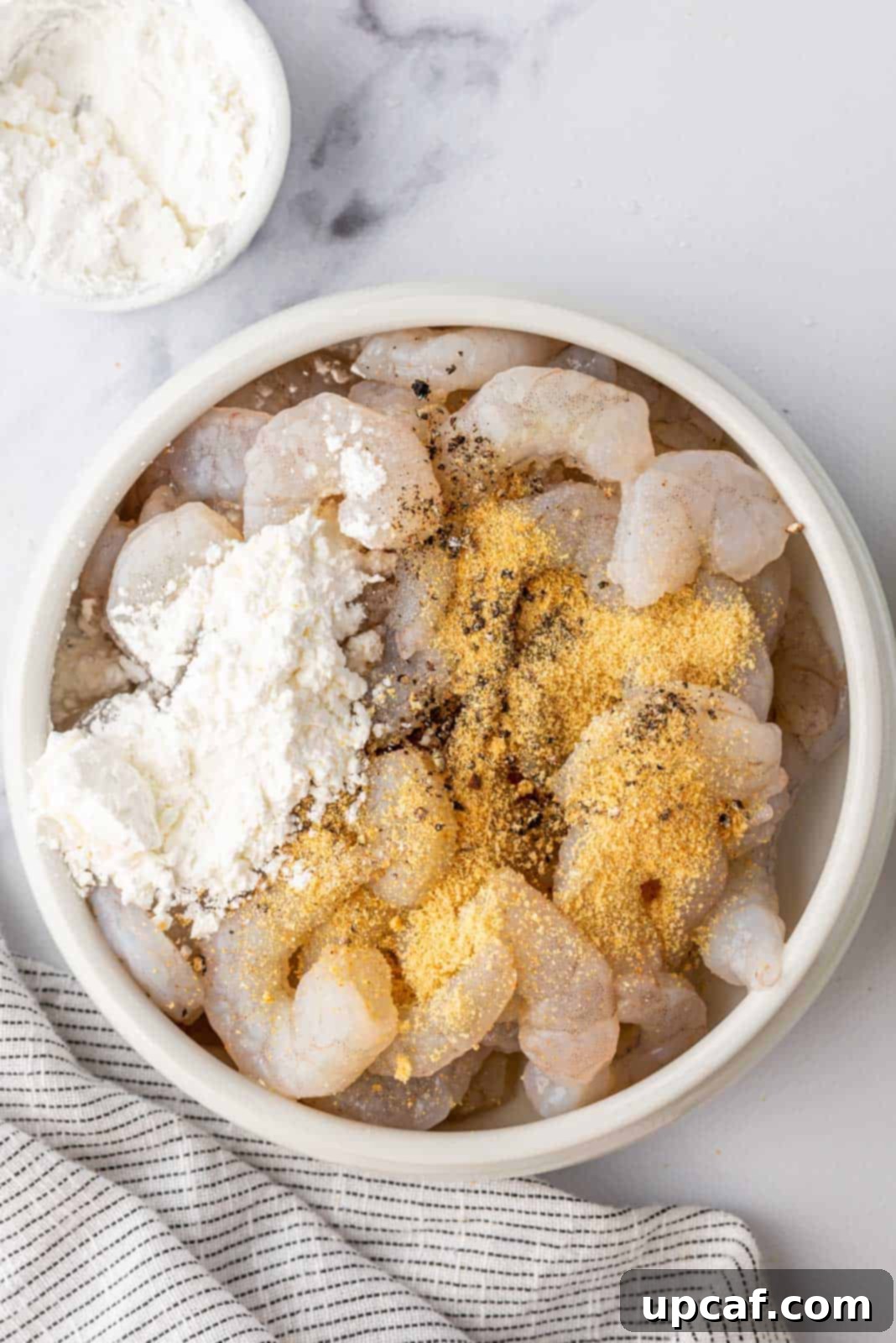 Raw shrimp being tossed in a bowl with a mixture of seasonings and cornstarch, preparing them for frying.