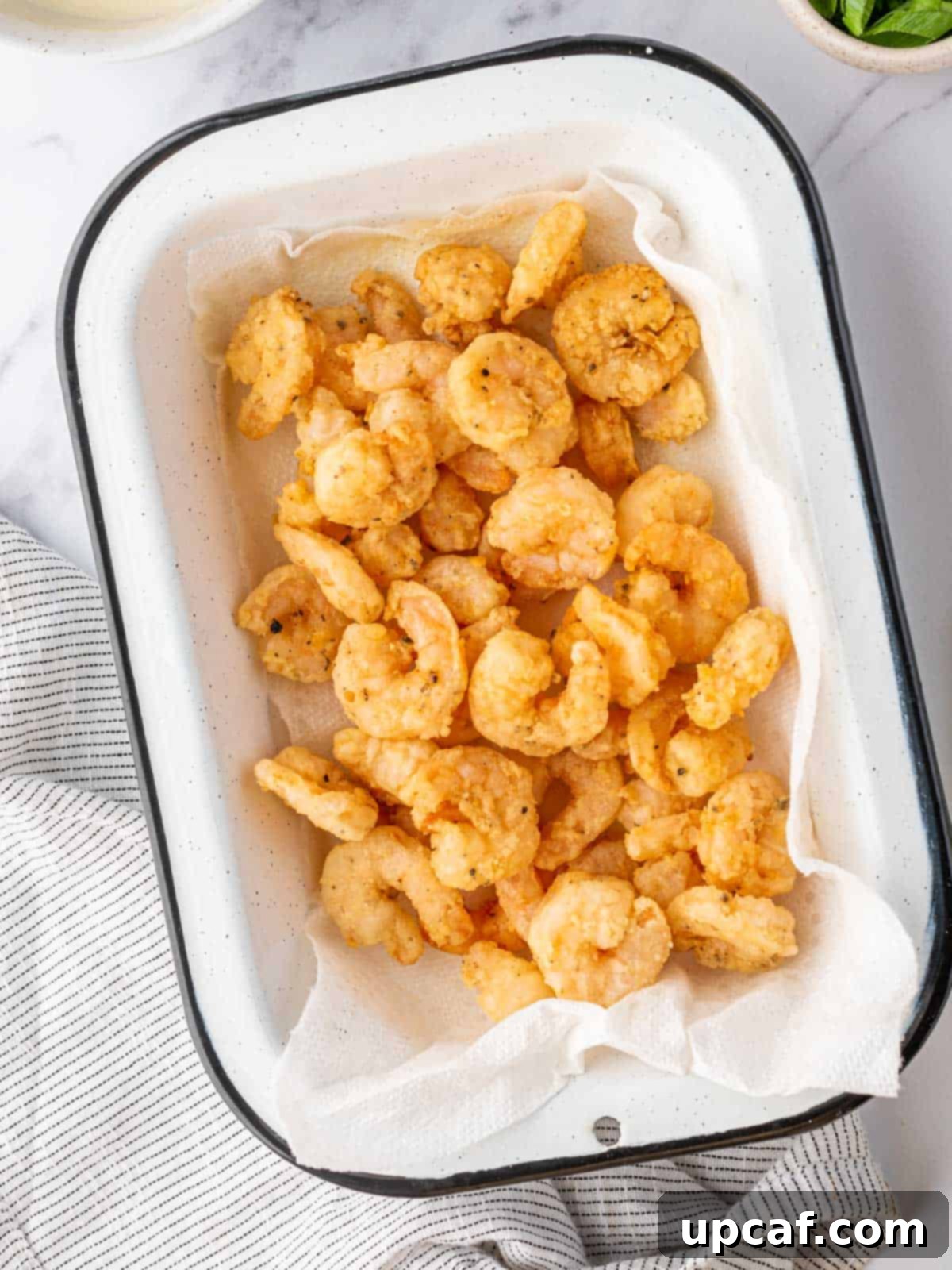 A batch of lightly fried, golden-brown shrimp resting on a plate, ready to be tossed with sauce and walnuts.