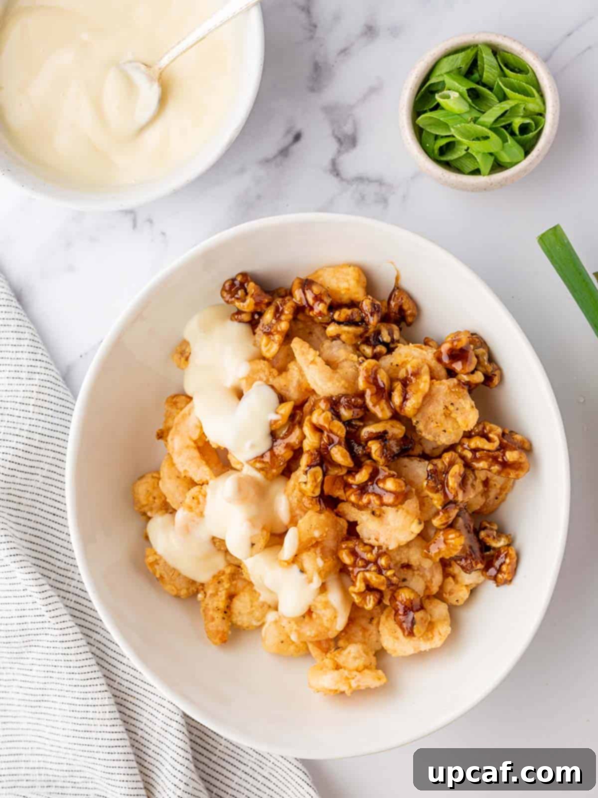 Fried shrimp, candied walnuts, and the creamy honey sauce being combined and gently tossed in a large bowl.
