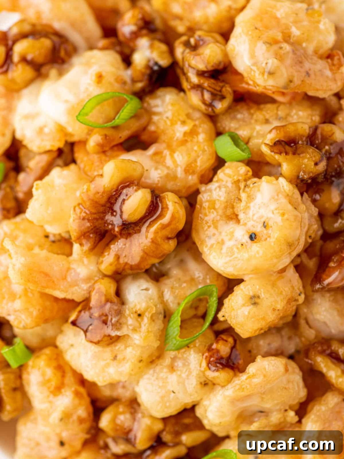 A delicious mound of crispy honey shrimp with candied walnuts and a sprinkle of green onions, presented beautifully.
