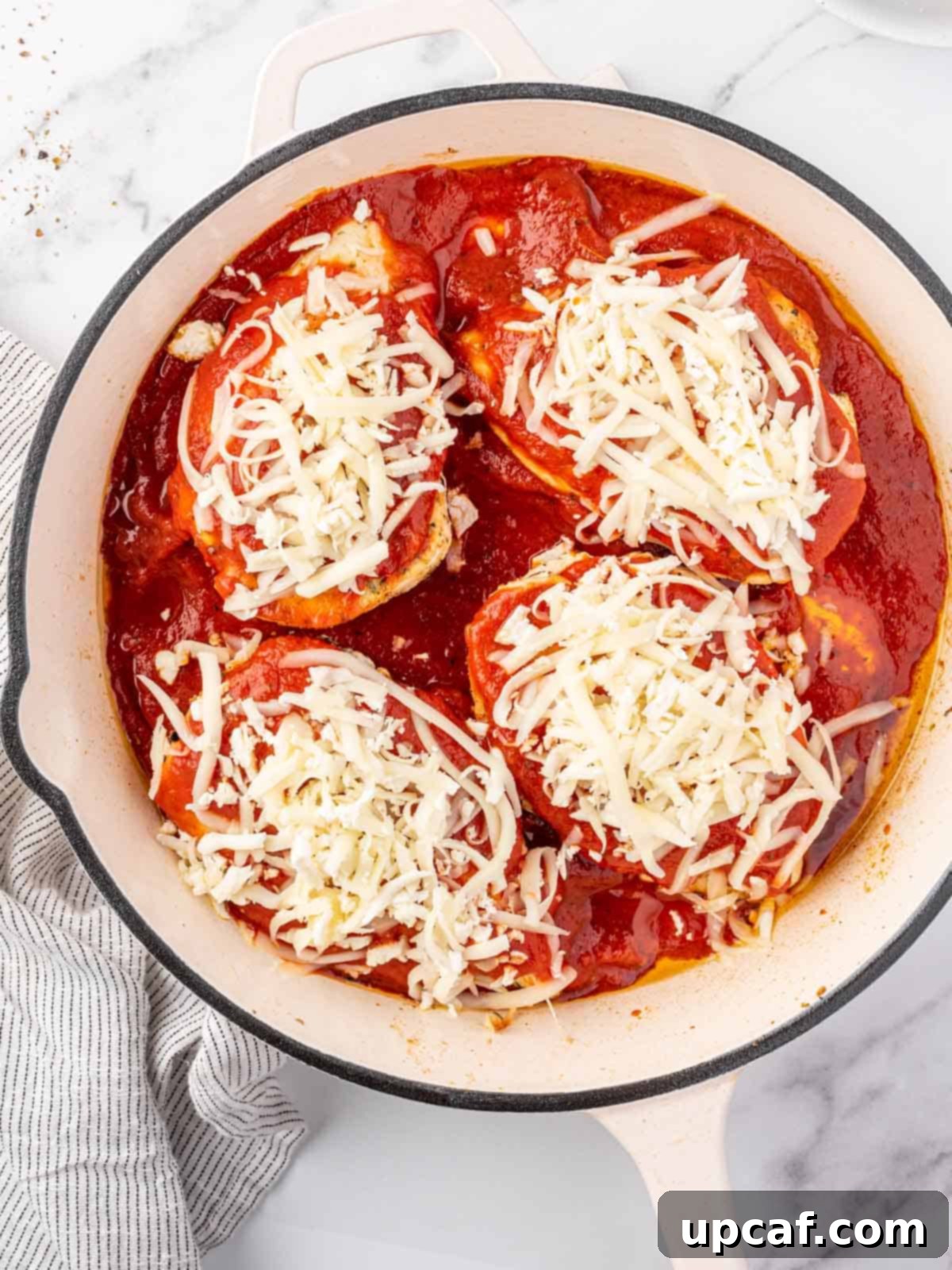 Keto Chicken Parm Skillet 7 Chicken breasts covered with marinara sauce and a generous layer of mozzarella cheese in a skillet, ready for baking.