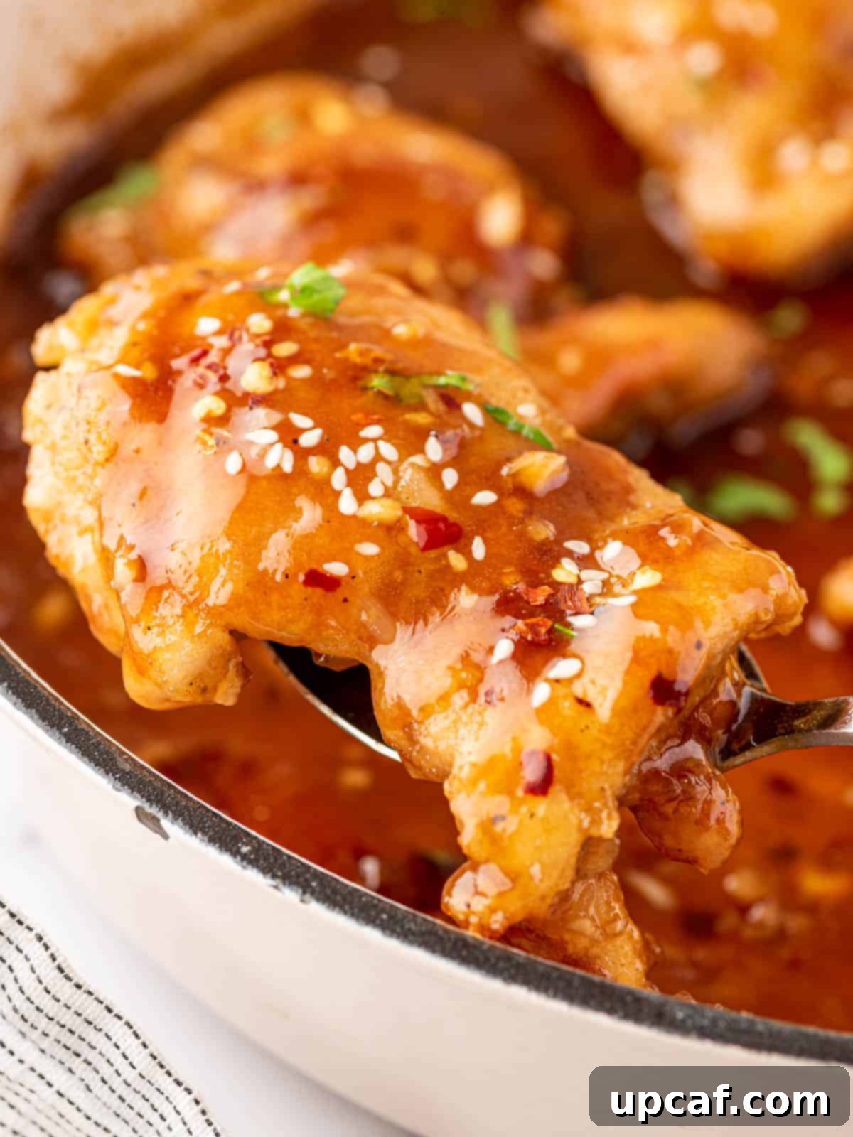 A honey garlic chicken thigh lifted with a spoon.