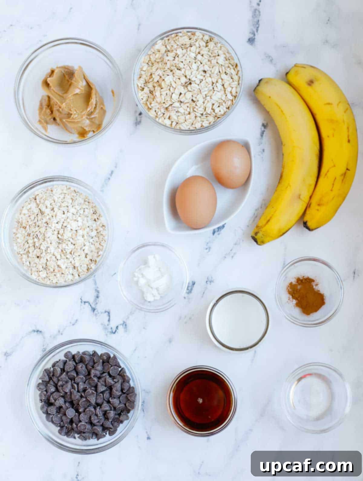 A flat lay photograph showcasing all the fresh and pantry ingredients needed to make homemade chocolate chip baked oatmeal, including oats, bananas, milk, eggs, and chocolate chips.