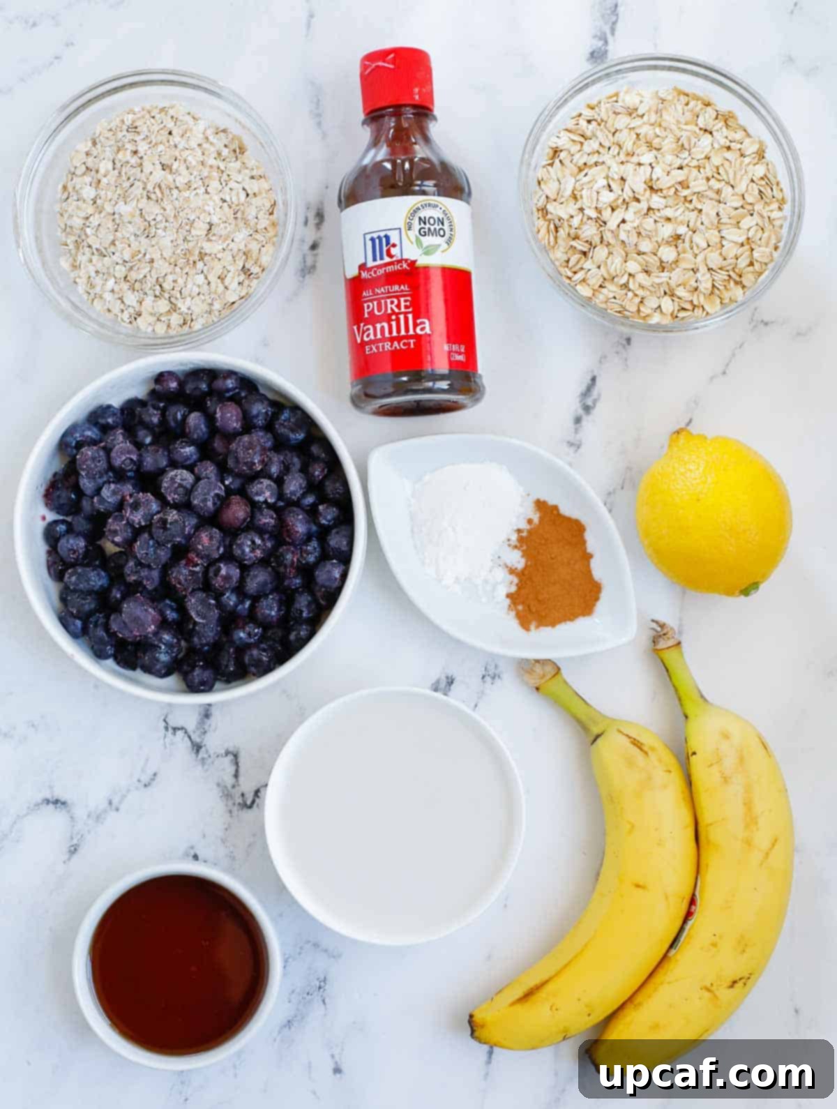 Hearty Blueberry Baked Oatmeal 3 A selection of fresh ingredients laid out on a kitchen counter, including rolled oats, quick oats, almond milk, maple syrup, ripe bananas, blueberries, cinnamon, vanilla extract, baking powder, salt, and a lemon, ready for making blueberry oatmeal bake.