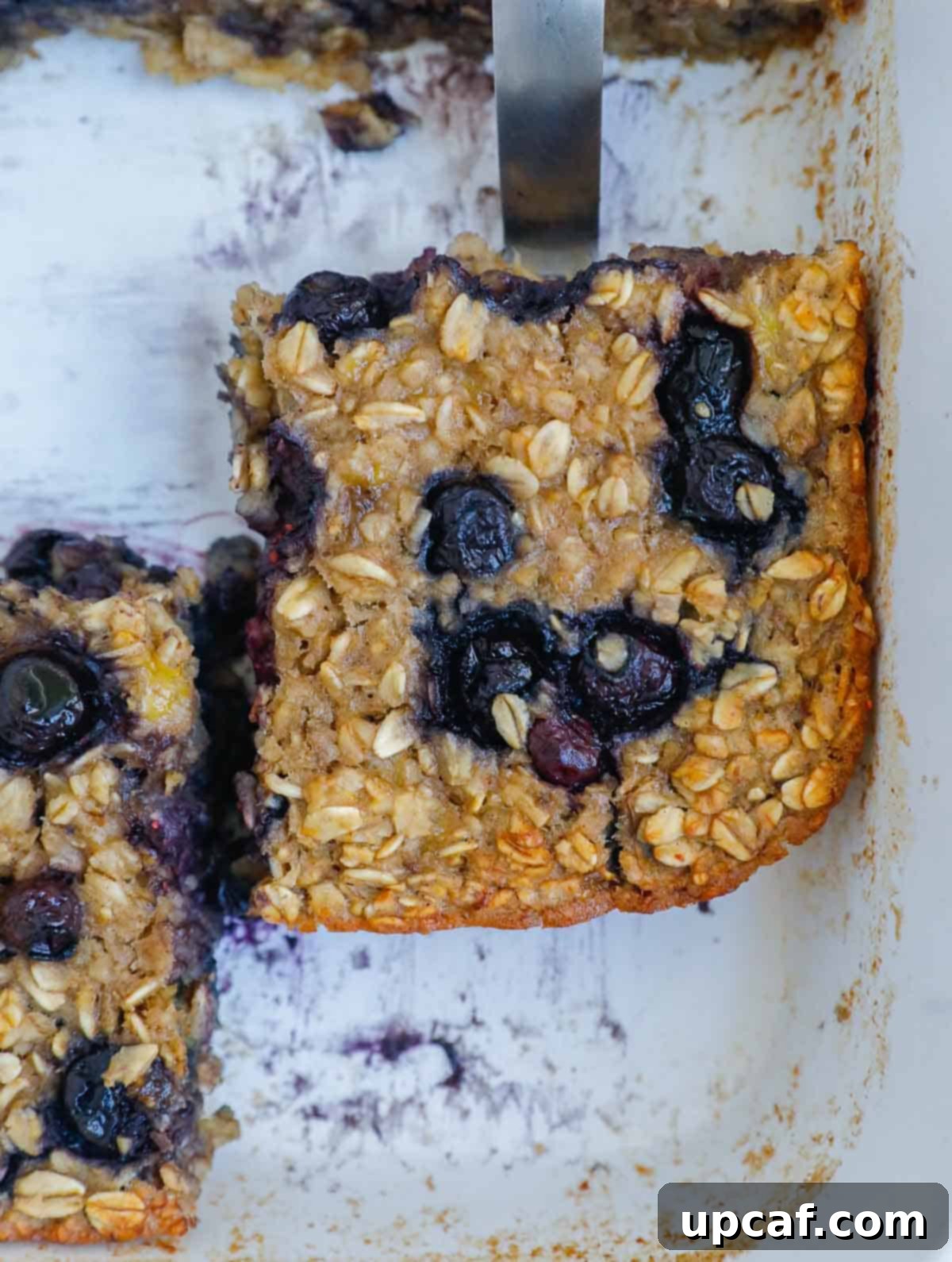 Hearty Blueberry Baked Oatmeal 8 A delicious slice of baked oatmeal, showcasing its golden crust and visible blueberries, served in a rustic dish, ready to be enjoyed.