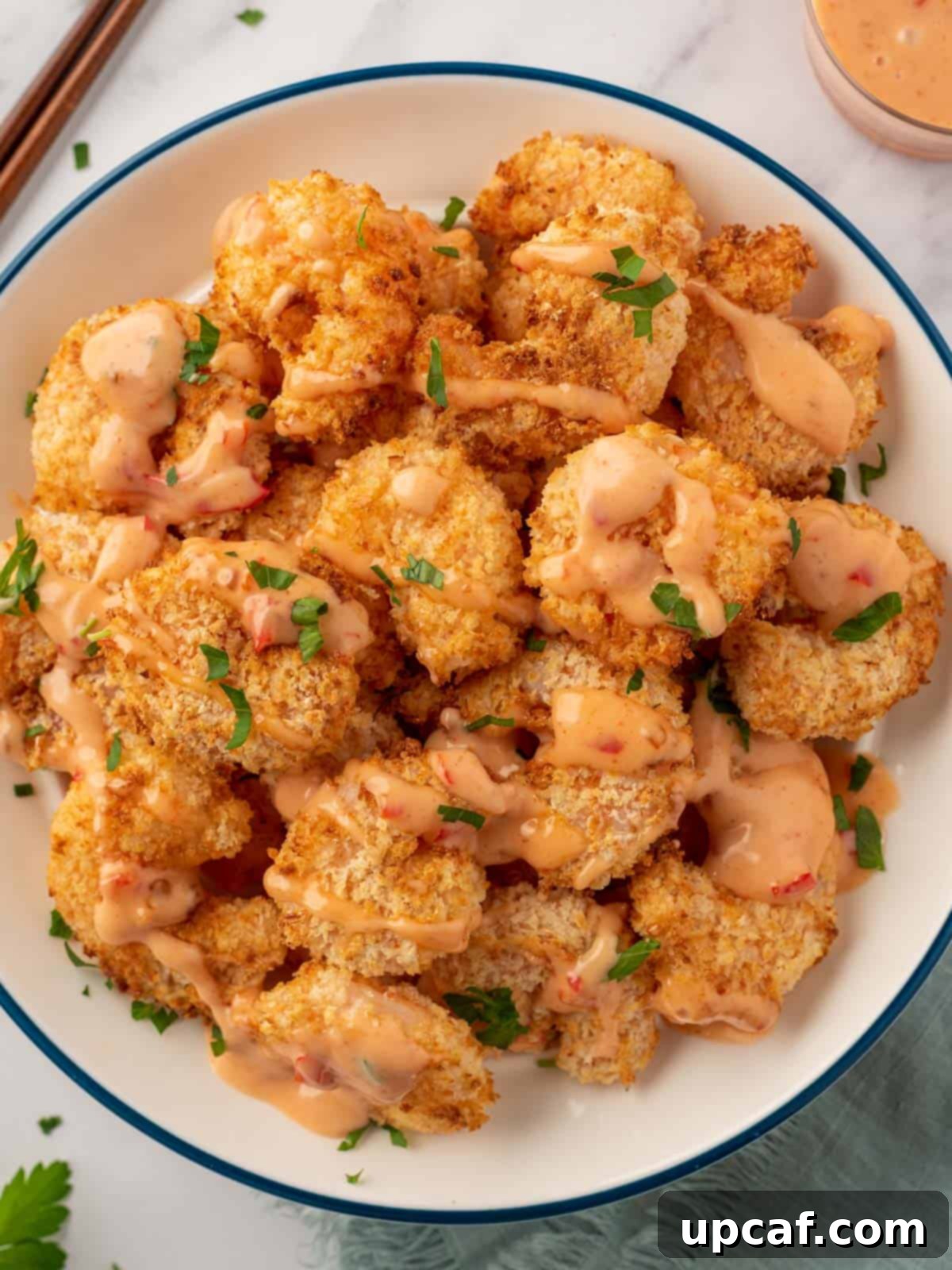 A pile of air fryer panko shrimp with bang bang sauce, garnished with fresh parsley.