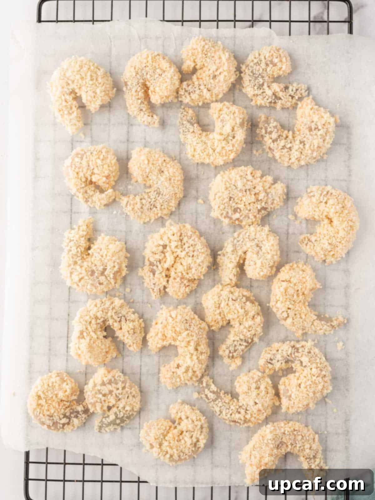Breaded shrimp neatly arranged on parchment paper, ready for air frying.
