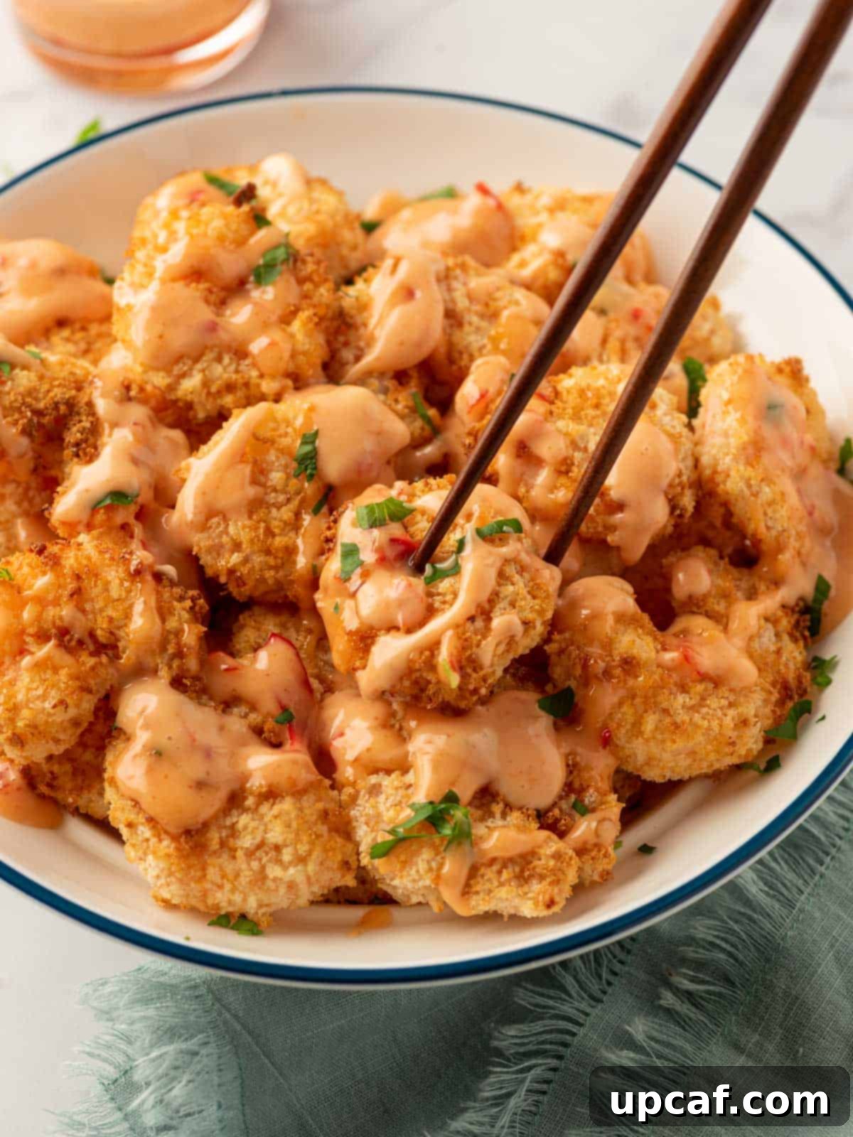 Bang-bang shrimp air fryer on a plate with chopsticks and bang bang sauce for dipping.