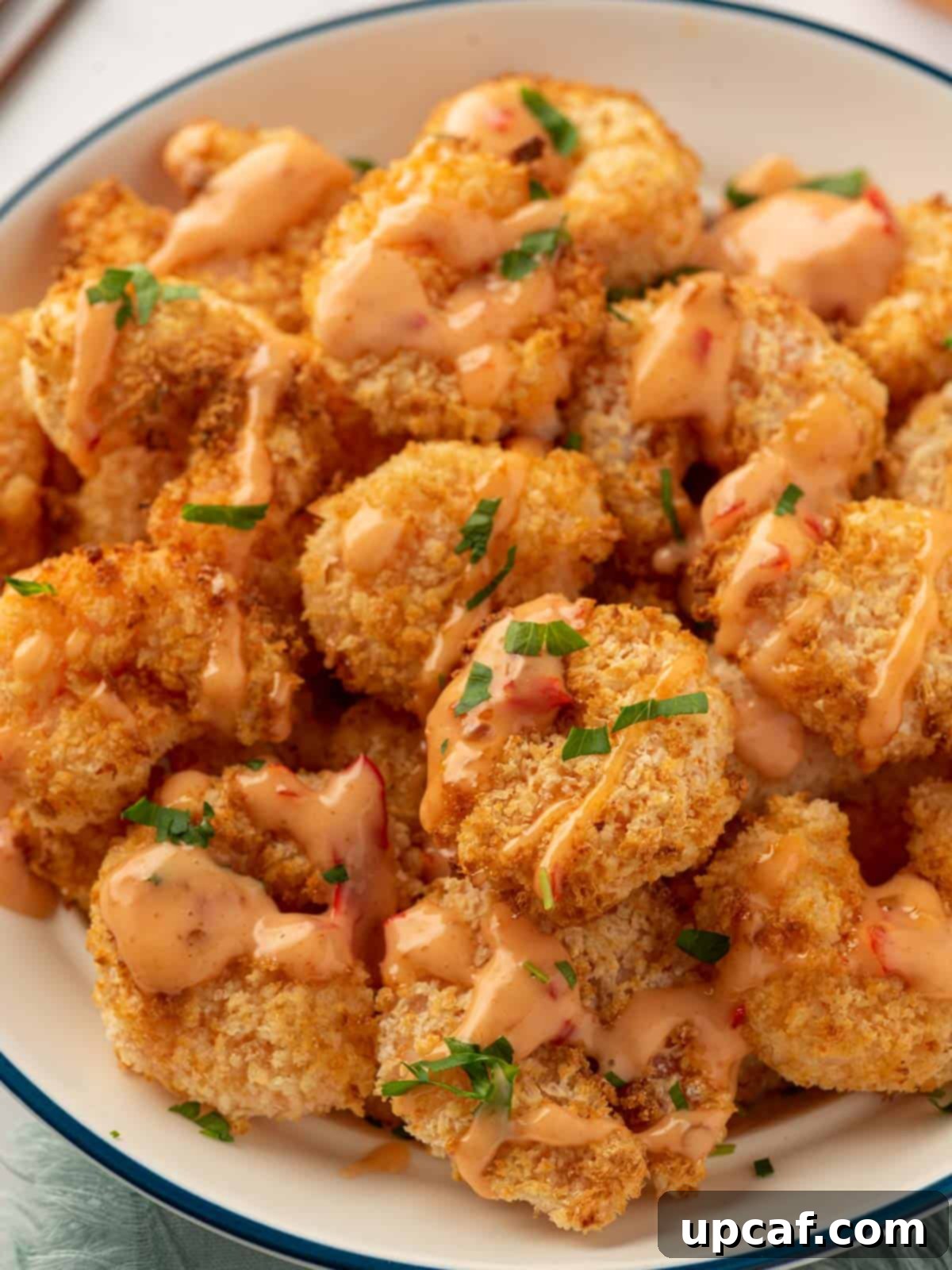 A plate of perfectly crispy air fryer panko shrimp generously drizzled with bang bang sauce.