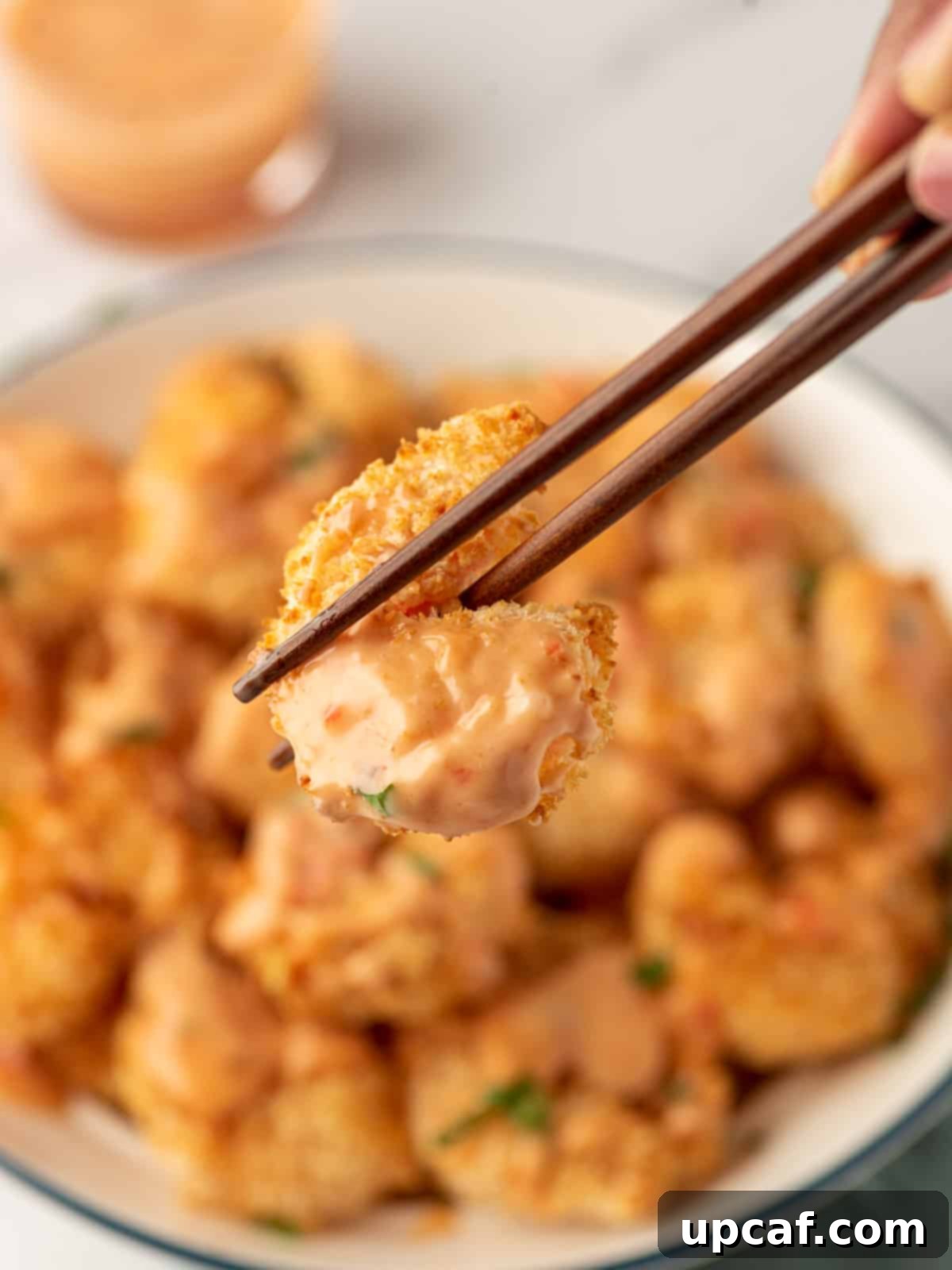 A single piece of crunchy air fryer bang bang shrimp held by chopsticks, ready to be eaten.