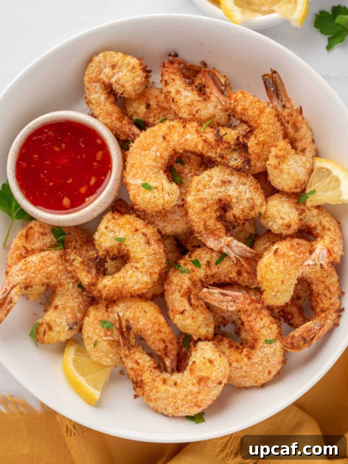 A delectable pile of golden-brown air fryer coconut shrimp, perfectly crispy, served on a plate with a side of sweet chili dipping sauce and fresh lemon wedges, ready to be enjoyed.
