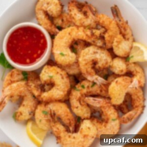 A pile of golden-brown air fryer coconut shrimp, perfectly crispy, served on a plate with a side of sweet chili dipping sauce and fresh lemon wedges.