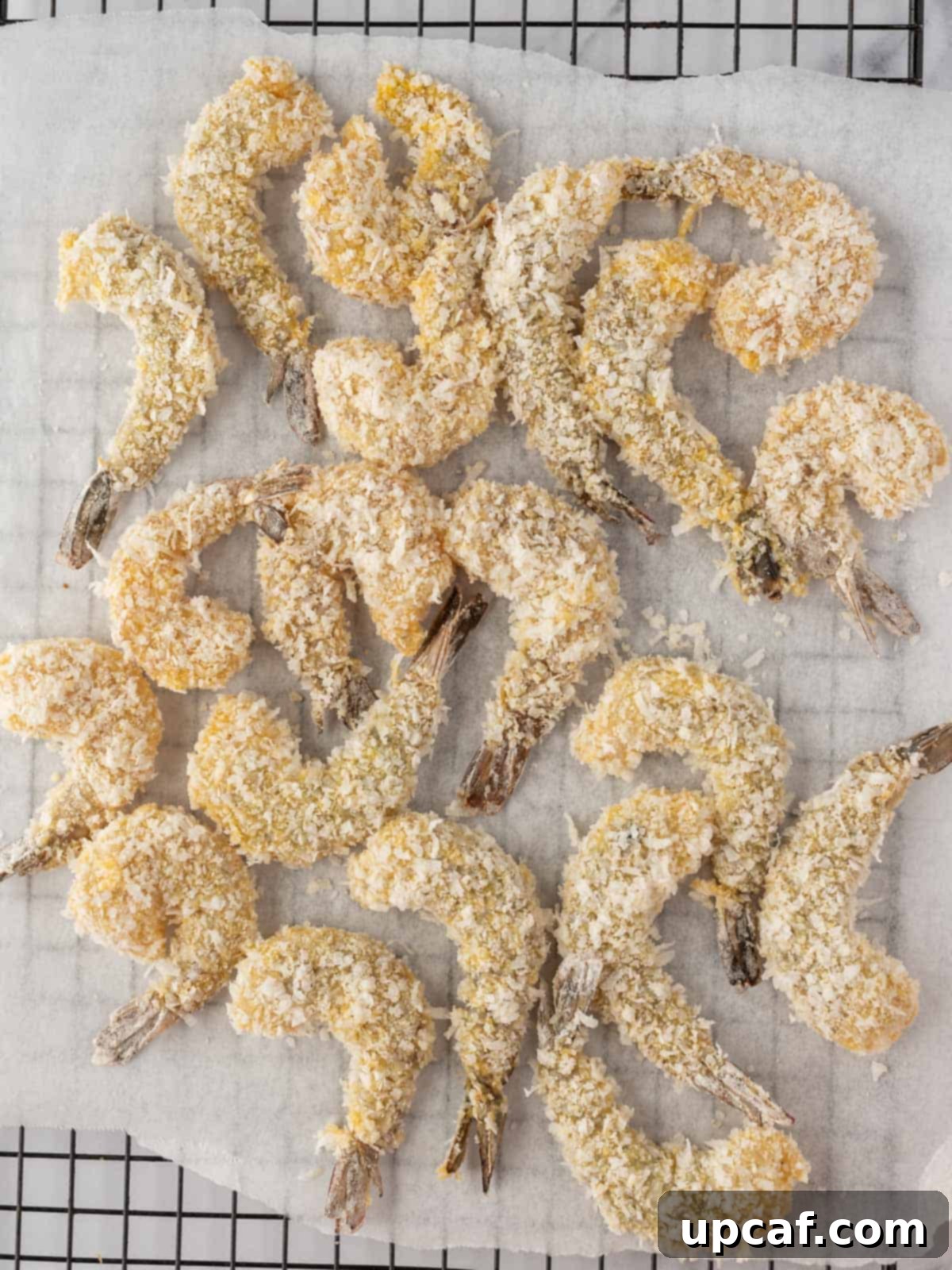 Many shrimp uniformly coated with coconut and panko breading, arranged neatly on parchment paper, waiting to be air fried.