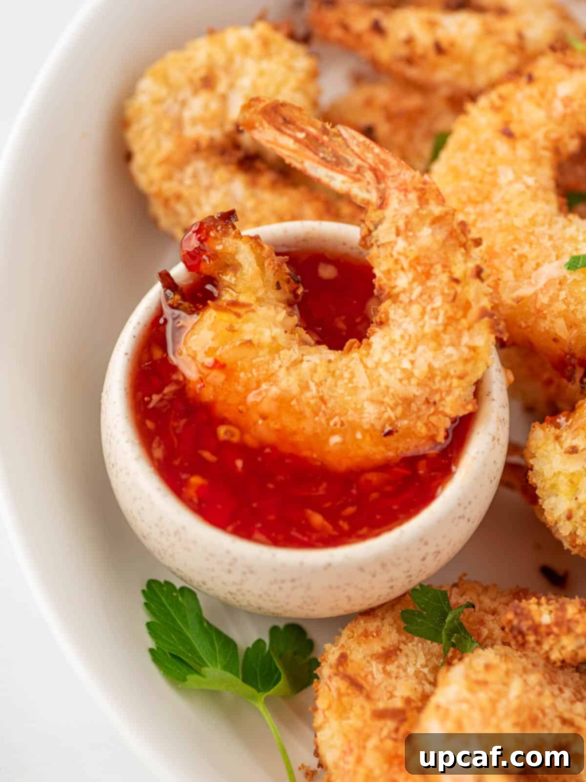 Crispy air fryer fried shrimp being dipped into a luscious sweet chili sauce, highlighting its golden texture and delicious pairing.