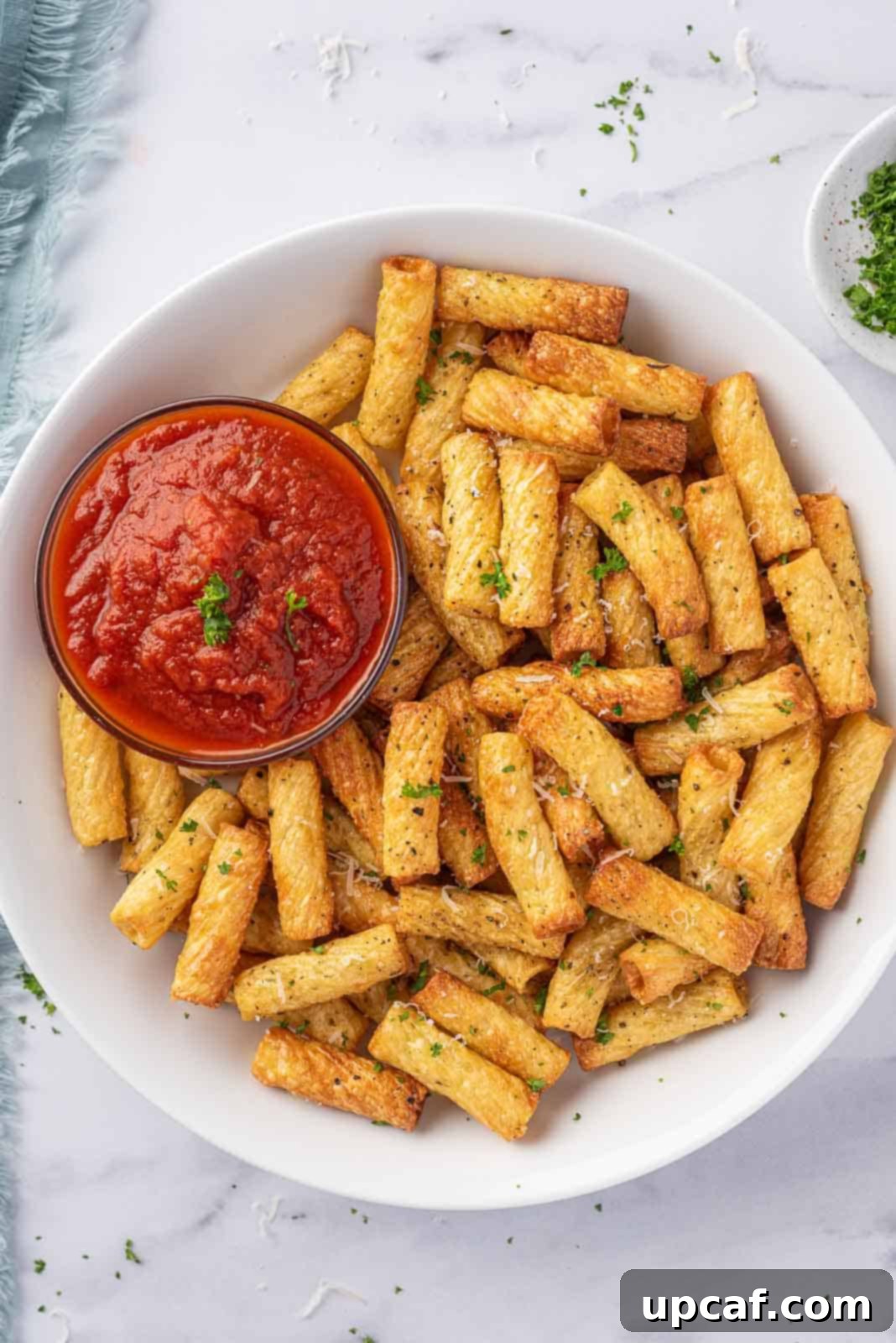 A plate of air fried pasta with a small bowl of marinara sauce.