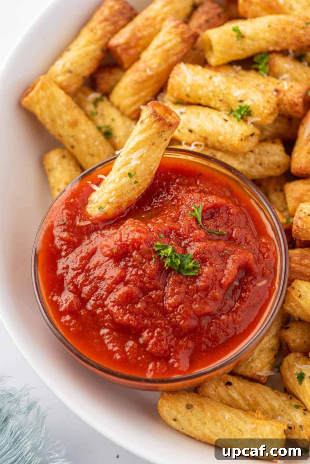 A plate of fried pasta chips and one fried noodle dipping into marinara sauce.