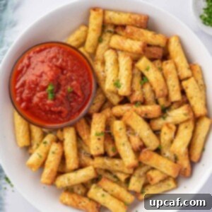 A plate of air fried pasta with a small bowl of marinara sauce.