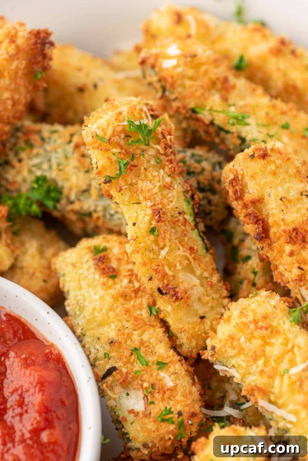 Close-up view of beautifully breaded and crispy zucchini fries on a serving platter.